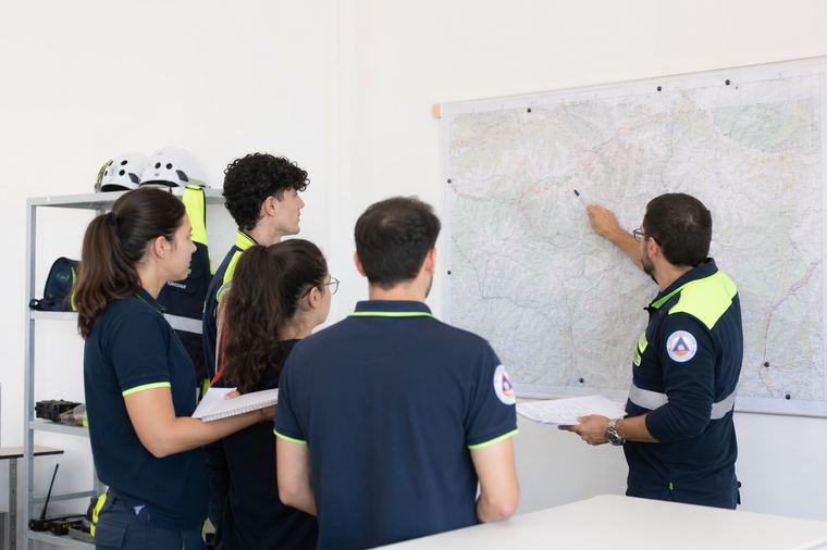 Gruppo di uomini con caschi neri e grigi riuniti accanto a un'auto scura, di giorno.